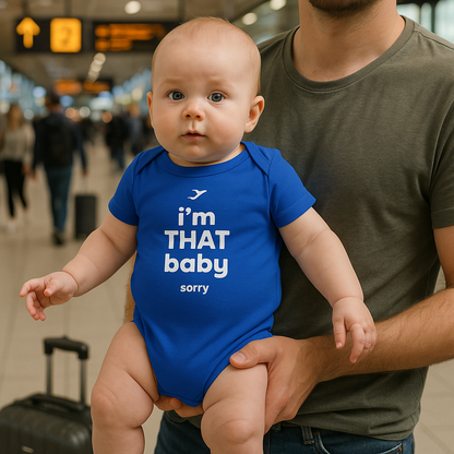 Baby wearing a blue onesie with text, held by a person in an airport.